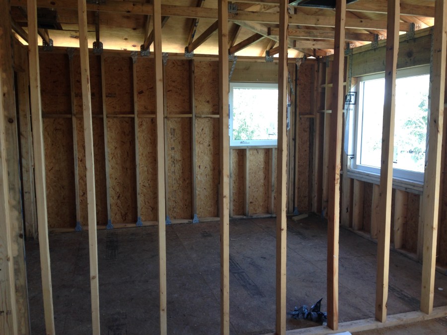 House under construction with wood framing exposed to show roof trusses, wall studs and plywood sheathing, with metal hurricane straps.

