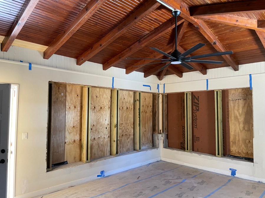 Interior of room under renovation with large corner window openings temporarily covered by plywood before windows installed