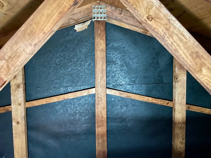 Gable end wall showing roofing felt behind siding in attic